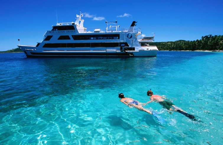 Turistahajó a háttérben, elől egy férfi és egy nő a vízben 