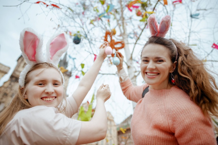 Boldog fiatal anya és tizenéves lánya húsvéti tojásokkal a városi vásáron feldíszített húsvéti fa előtt.