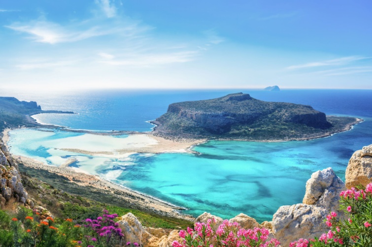 Kék vizű tengeröböl fehér sziklákkal és virágokkal.