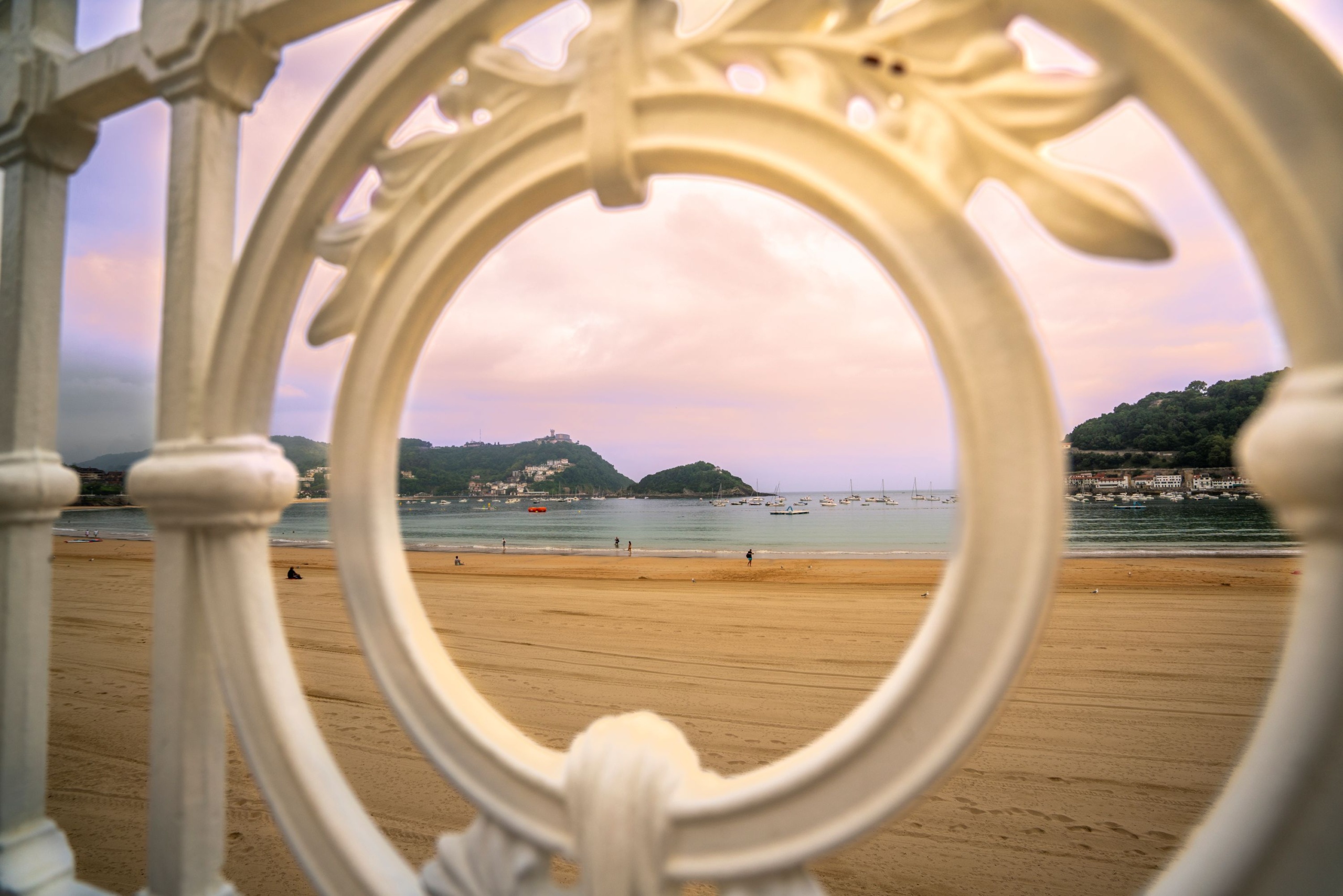 A fehér korlát egy részlete, mögötte a homokos tengerpart.