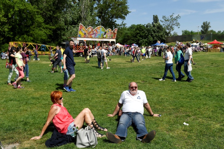 Fűben ülő emberek, a háttérben vidámparki elemek.