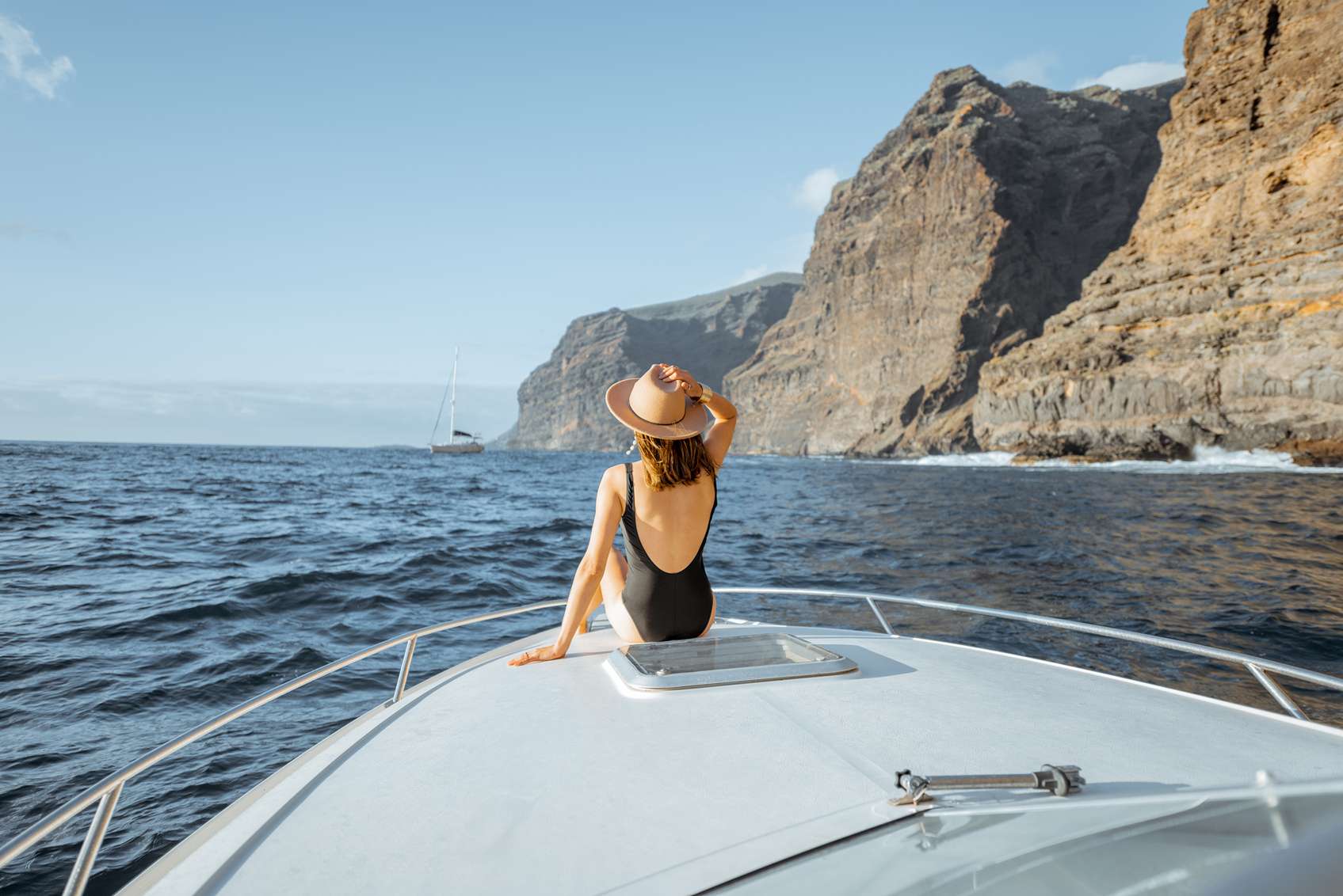 Fürdőruhás kalapos nő hajón ül