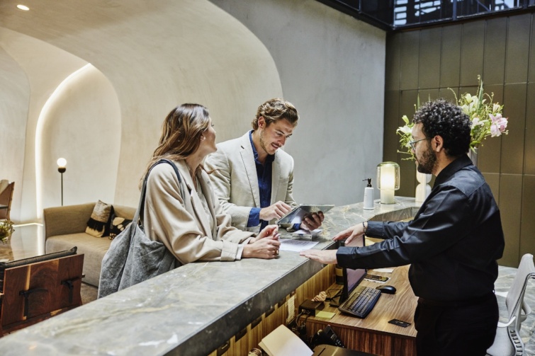 Fiatal pár áll egy szálloda recepciójánál, és intézik a bejelentkezést 
