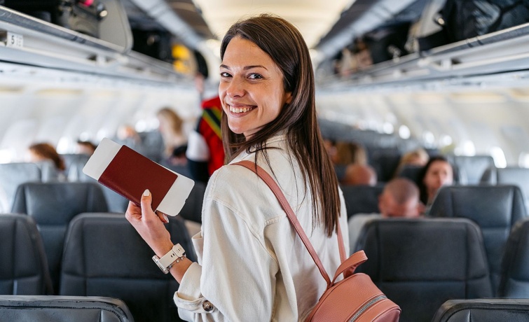 Young Woman Boarding An Airplane - Startlap Utazás Egy mosolygó fiatal nő útlevelet tart a kezében a repülőgép utasterében.