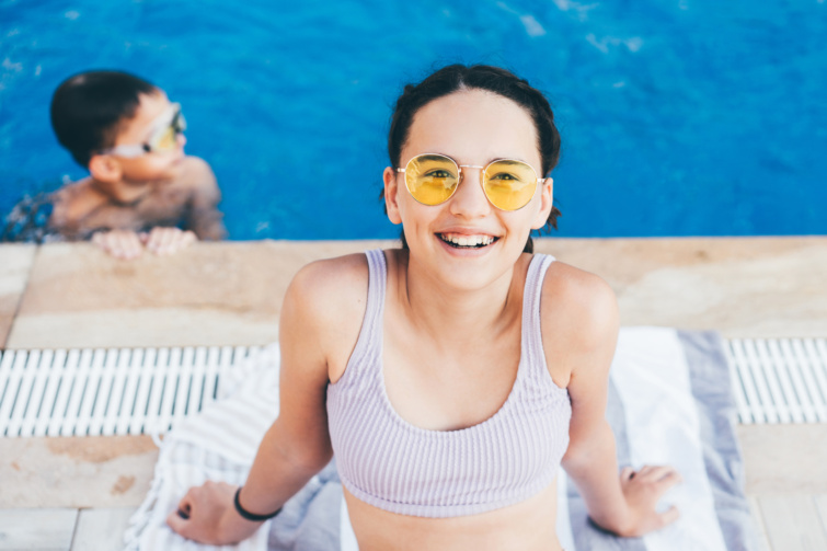Kislány mosolyog egy medence partján bikiniben