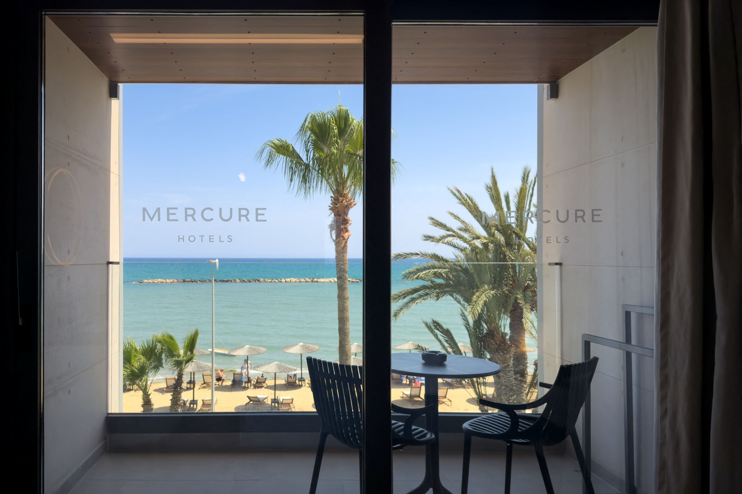 A Mercure Larnaca Beach Resort tengerre néző szobája egy erkélyre nyílik, ahonnan pálmafákra, a strandra és a Földközi-tengerre nyílik kilátás Orokliniben, a Larnaca kerületben, Cipruson