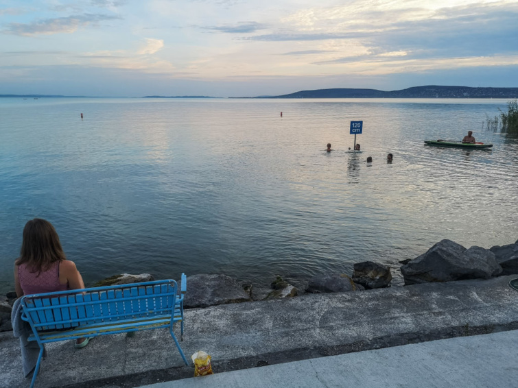 Fiatal nő egy padon ülve nézi a Balatont