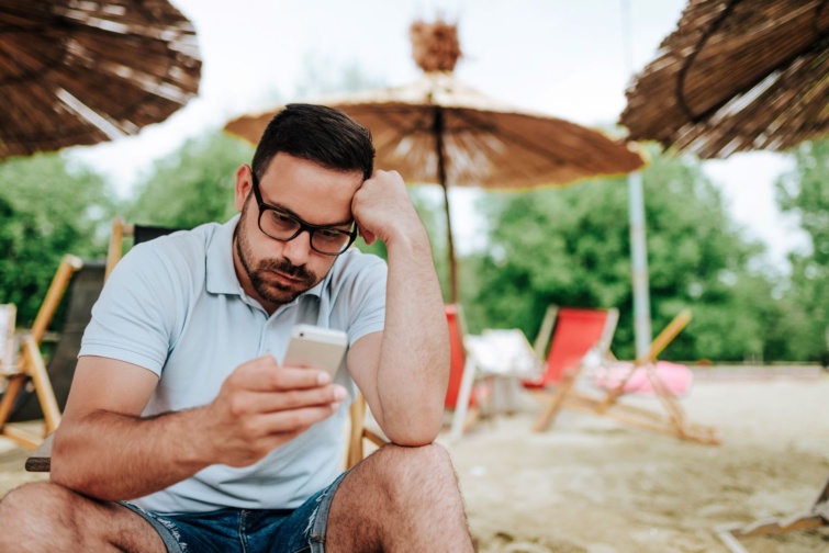 stressz strand - Startlap Utazás Stresszes férfi nézi zaklatottan a telefonját a strandon.