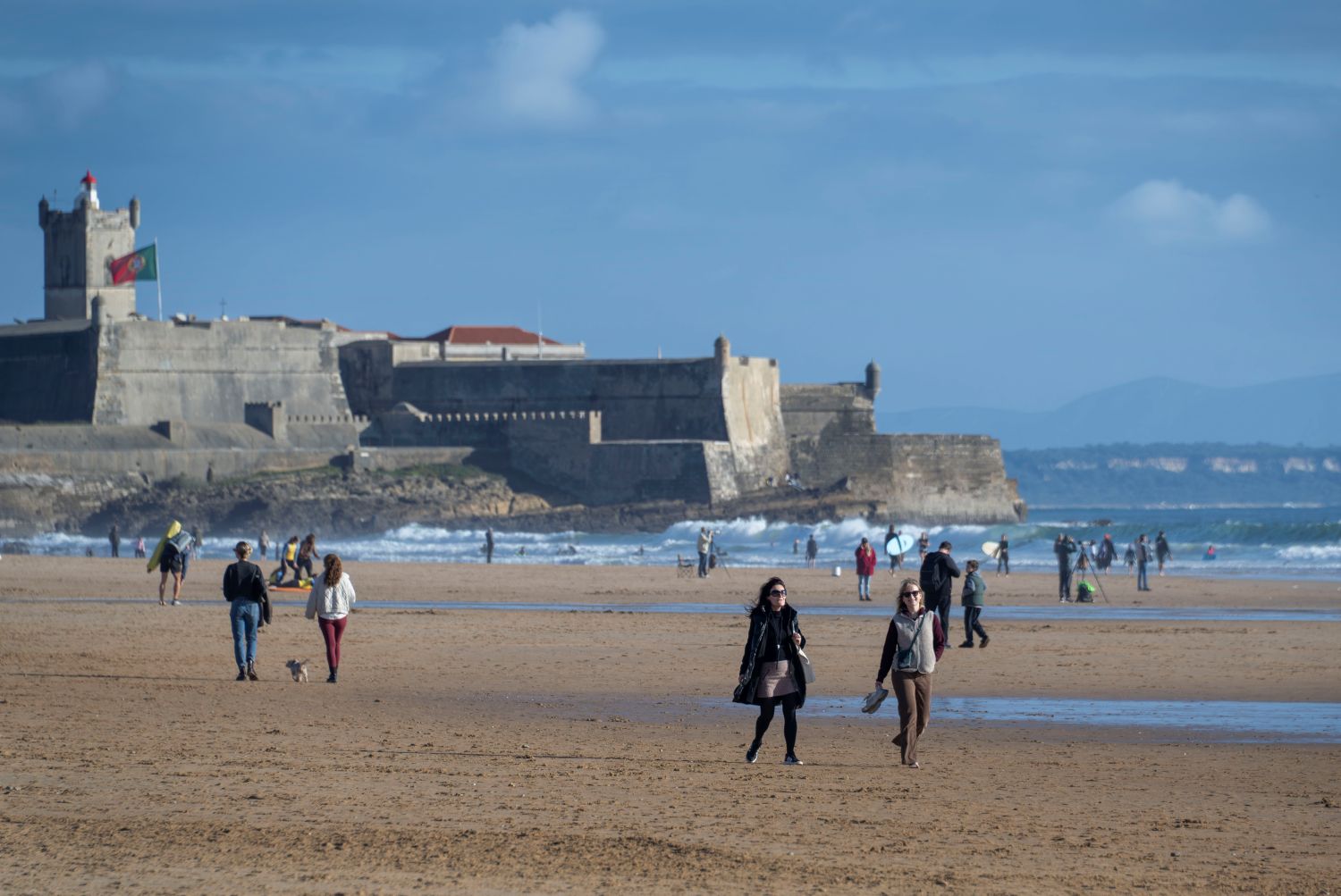 Carcavelos homokos strandján sétálnak a helyiek.