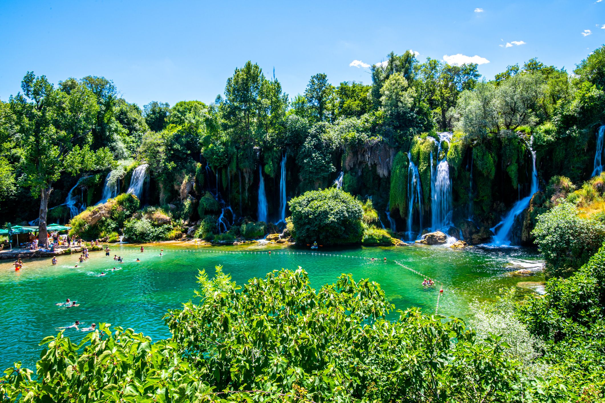 Panorámakép a Kravica-vízesésről; a vízesést a Trebišnjica folyó alakította ki, amely mély medencébe zúdul alá, lélegzetelállító látványt és egyben kiváló nyári fürdőhelyet kínálva.