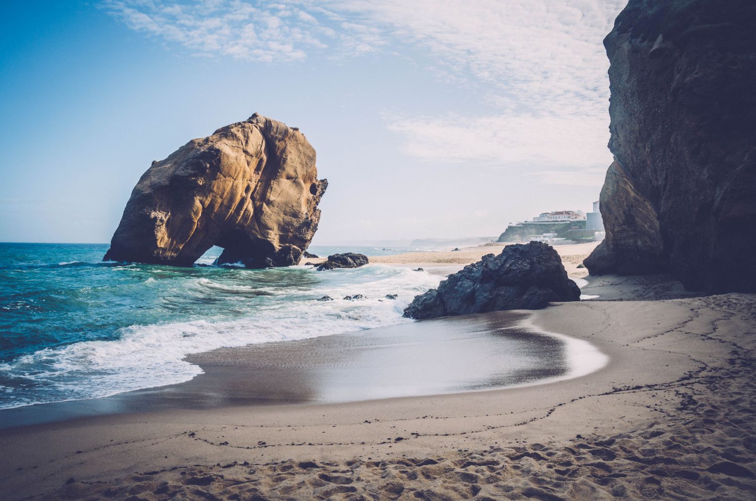 Penedo do Guincho festői partja. A képen hatalmas szikla látható a vízben és a világoskék tenger.