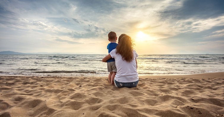 Mother with son enjoying sunset on the beach - Startlap Utazás Egy anya és kisgyereke háttal a kamerának a homokos strandról a tengert nézi.