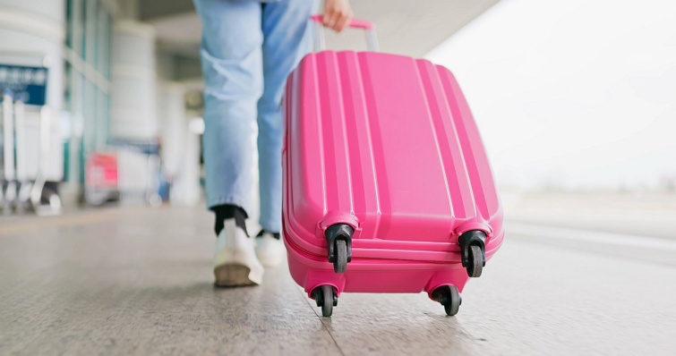 close up dragging suitcases airport - Startlap Utazás Egy kerekes, pink bőröndöt húz egy alak.