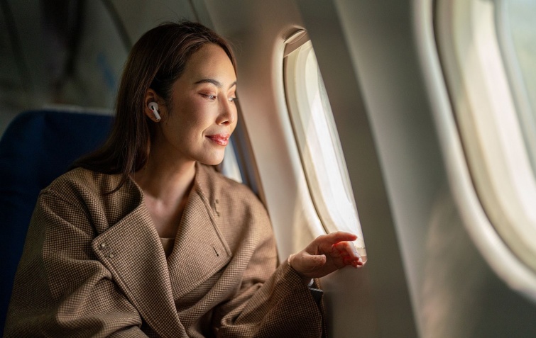 Businesswoman using phone while travelling on a flight - Startlap Utazás Fiatal ázsiai nő fülhallgatóval kinéz egy repülőgép ablakán.