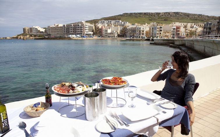 Food Kartell restaurant Marsallforn Gozo Malta - Startlap Utazás Egy nő bort iszik egy tengerparti étterem teraszán..