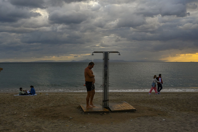 Felhős az ég egy görög strandon, a kép középpontjában egy férfi zuhanyzik