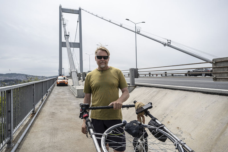 bushby - Startlap Utazás napszemüveges férfi egy hídon kézikocsival