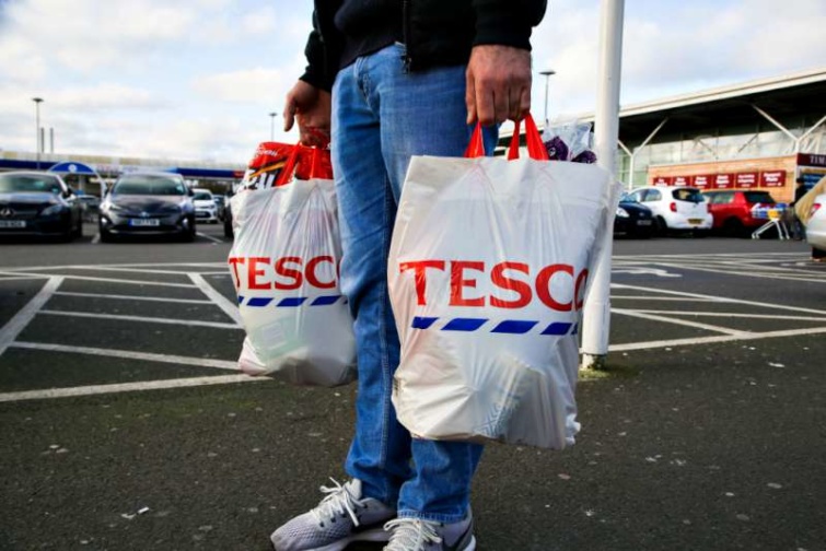 A shopper carries Tesco shopping bags as he leaves a Tesco Startlap Vásárlás