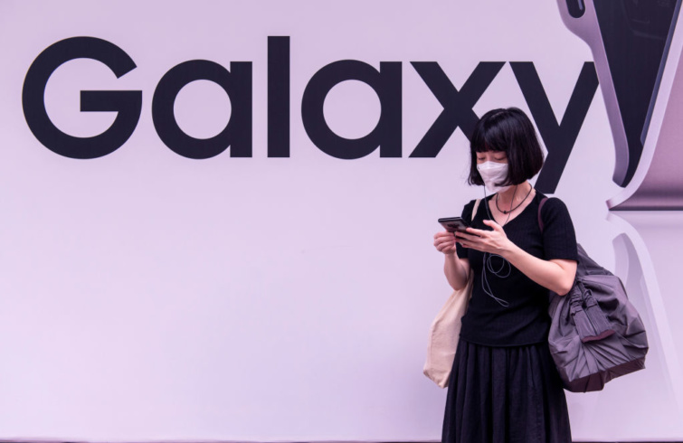 Okostelefonozó nő egy Galaxy felirat előtt.