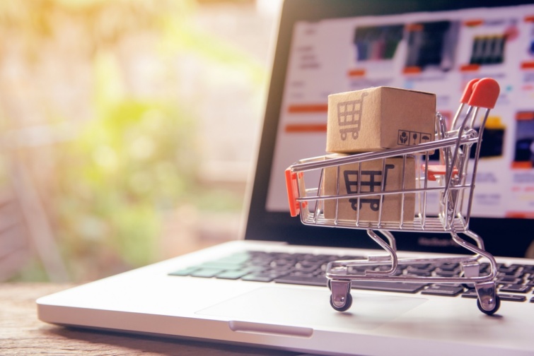 Illusztráción az online vásárlás: egy laptop és egy miniatűr bevásárlókosár 
