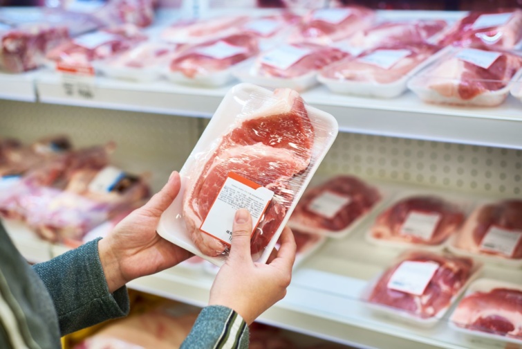 Egy vásárló egy csomagolt sertéshústerméket tart a kezében a boltban.