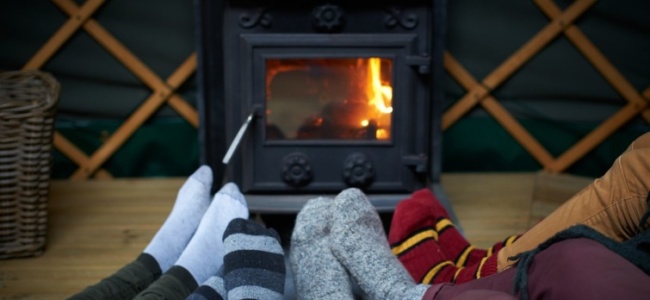 Zokniba bújtatott lábak melegednek egy kályha előtt, melyben pattog a tűz