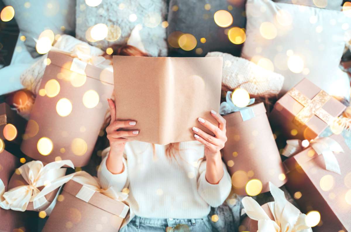 Karácsonyi ajándékok között olvas könyvet egy nő