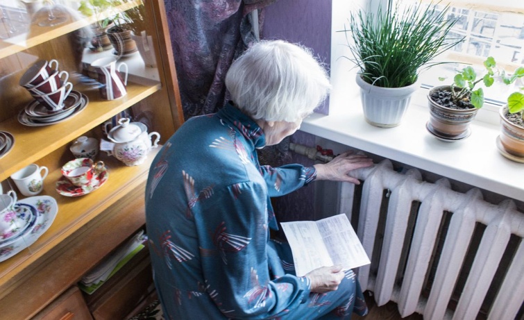 Egy nyugdíjas nő a radiátort érinti, kezében számla.