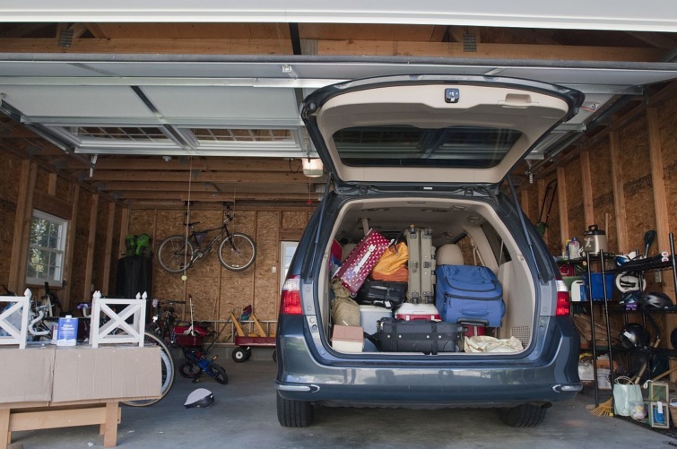 Nyitott csomagtartójú, bőröndökkel megpakolt autó áll egy garázsban.