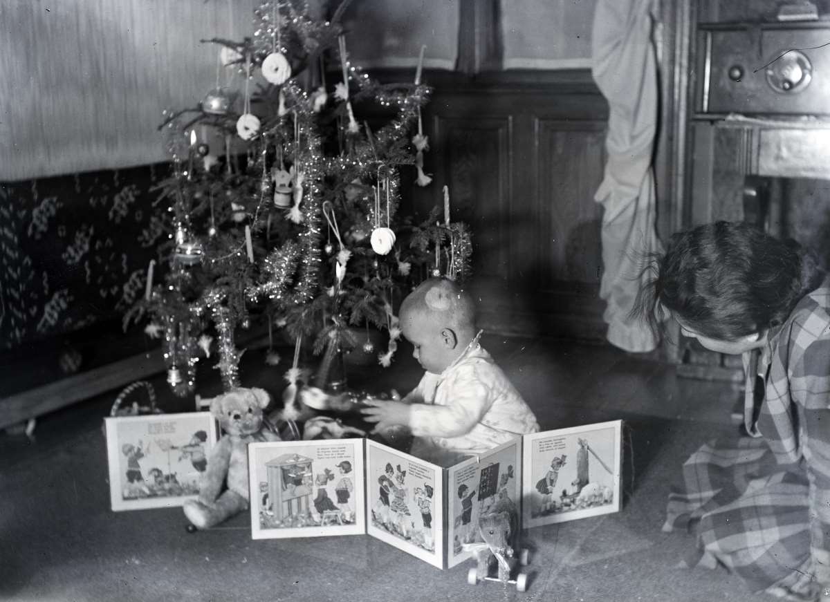 Leporelló előtt guggoló kisgyerek a karácsonyfa mellett