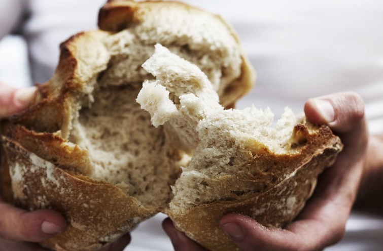 Egy félbetört kenyér egy ember kezében.