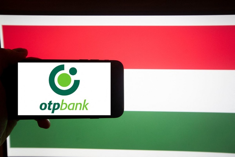 Az OTP Bank logója egy mobiltelefon kijelzőjén, a háttérben a magyar zászló.