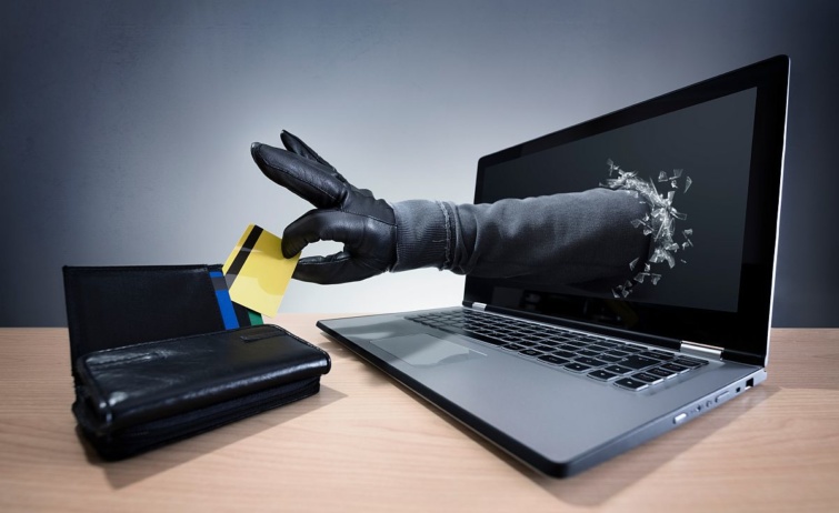 Adathalászat: egy, a laptop képernyőjéből kinyúló kesztyűs kéz bankkártyát emel ki egy pénztárcából.