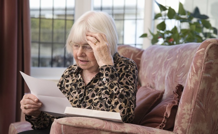 Egy fotelben ülő, szemüveges, idős nő levelet olvas.