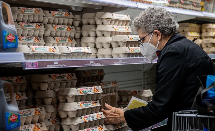 Egy arcmaszkot viselő idős nő tojást vásárol a boltban.