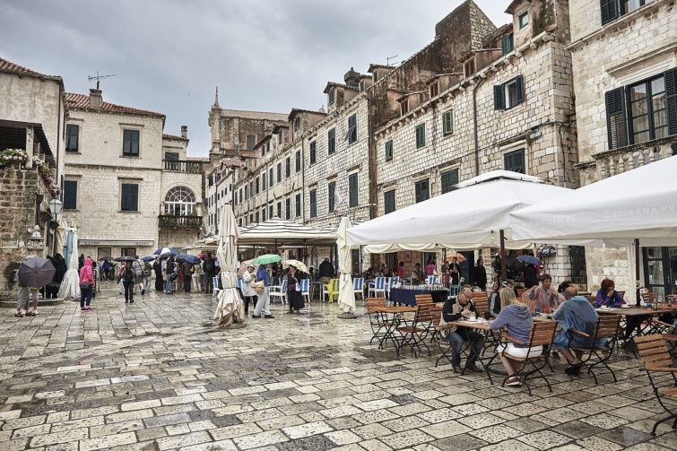 Dubrovnik egyik tere turistákkal és éttermi teraszokkal.