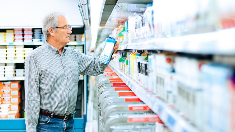Egy férfi vásárló egy tejesdobozt vizsgál a szupermarketben.