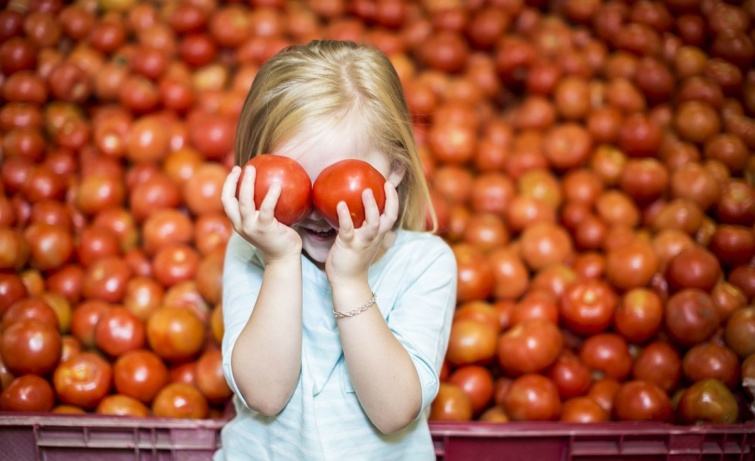 Egy gyerek két paradicsomot tart a szemei előtt a boltban.