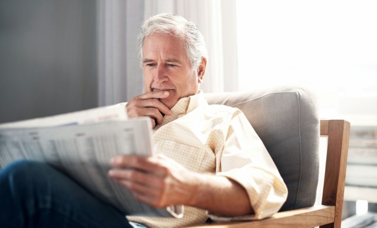 Egy fotelban ülő idős férfi újságot olvas.