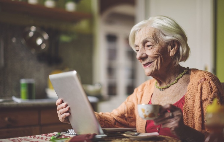Egy idős nő egy tabletet tartt egyik kezében, a másikban egy kávés csésze.