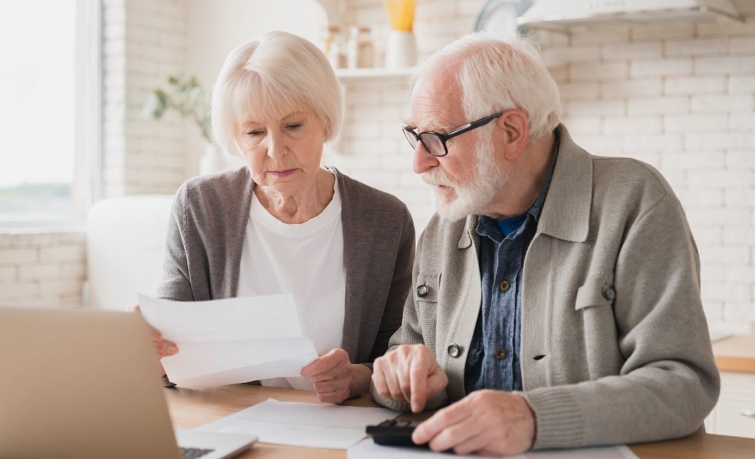 Egy nyugdíjas nő és egy nyugdíjas férfi egy iratot néz és számológépet használ.