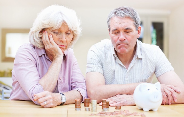 Szomorú nyugdíjas pár nézi az asztalon álló malacperselyt és a pénzérméket.