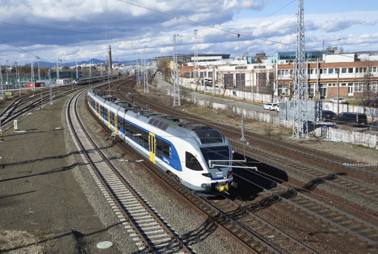 A MÁV Start Zrt. Stadler Flirt típusú zónázó személyvonata halad a Keleti pályaudvarról induló vasúti fővonal vágányain az Asztalos Sándor utca mellett. A pályaudvar négy fő vasútvonal: Budapest–Győr–Bécs (1-es), Budapest–Hatvan–Miskolc (80-as), Budapest–Szolnok-Békéscsaba–Arad (120-as), valamint a Budapest–Kelebia–Belgrád (150-es) vonalak kiindulópontja. Háttérben a Puskás Aréna és a Kerepesi úti úgynevezett Százlábú közúti híd a vasúti vágányok felett.