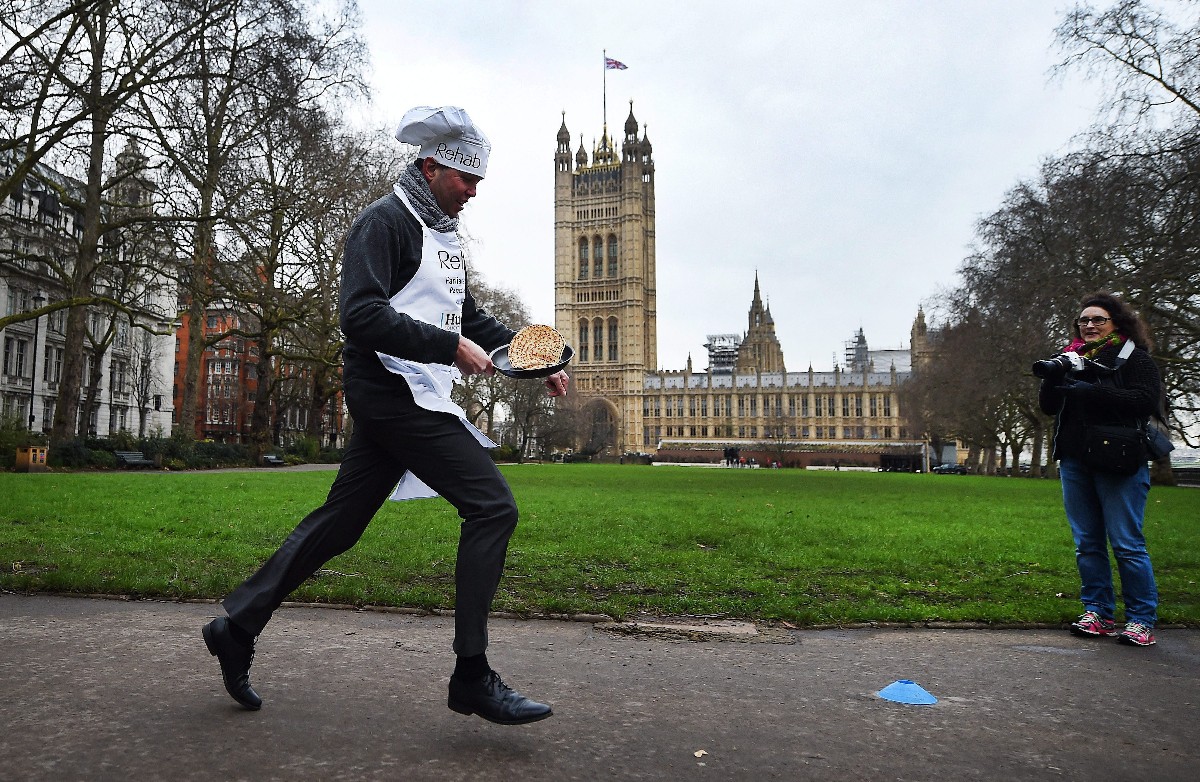 Egy brit parlamenti képviselő palacsintát forgat egy palacsintasütőben, miközben fut, hogy mielőbb célba érjen a londoni Victoria Tower Gardensben rendezett jótékonysági ügyességi versenyen 2016. február 9-én.