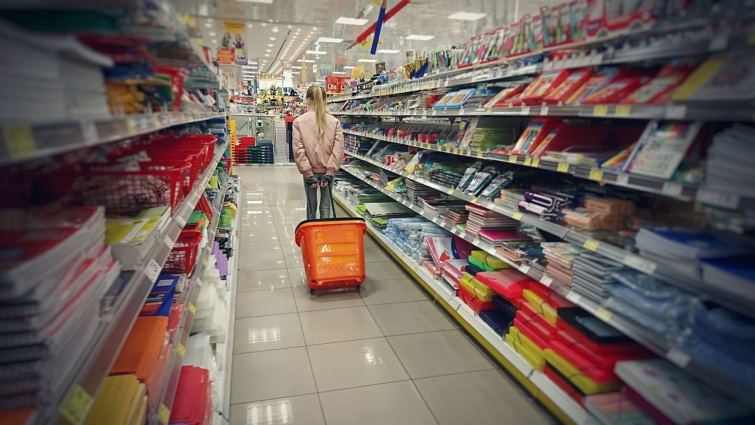 Egy lány egy bevásárlókosarat húz maga után a boltban a taneszközös termékek között.