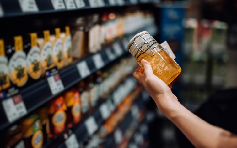 Egy vásárló egy üveg mézet tart a kezében a boltban.