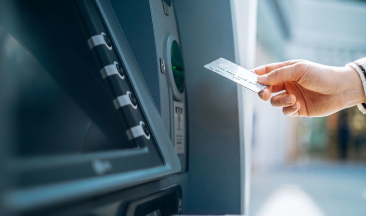 Bankkártyát tart egy kéz egy bankautomata előtt.