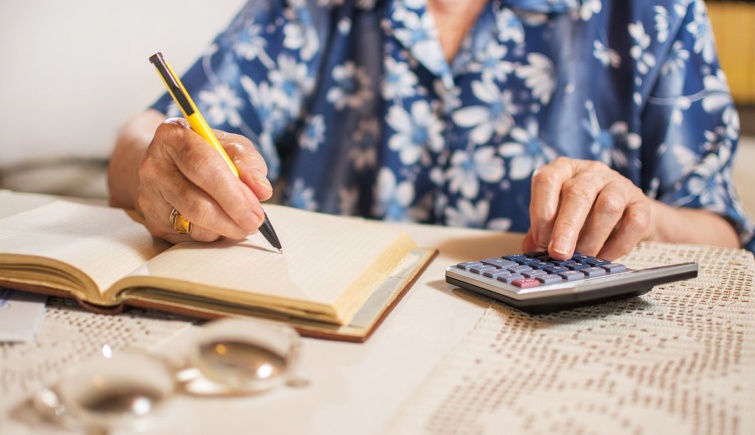 Egy nyugdíjas egy füzetbe ír és számológépen számol.