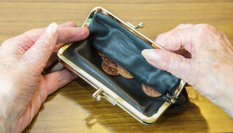 Egy nyugdíjas egy kinyitott pénztárcát tart a kezében, benne némi aprópénz.