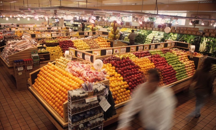 Zöldséges és gyümölcspultok egy szupermarketben elmosódó vásárlókkal.